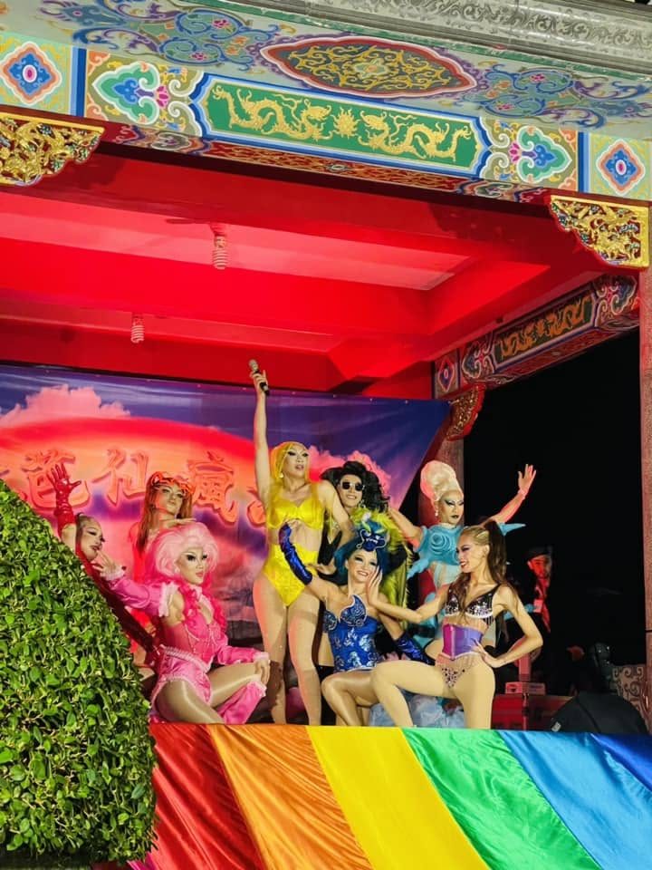 2023 年台北石牌福佑宮前的《彩虹芭仙傳》演出，七位變裝皇后站在廟埕舞台上，台前掛著彩虹旗